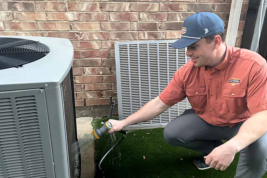 Brothers technician rinsing an outdoor condenser coil with a hose