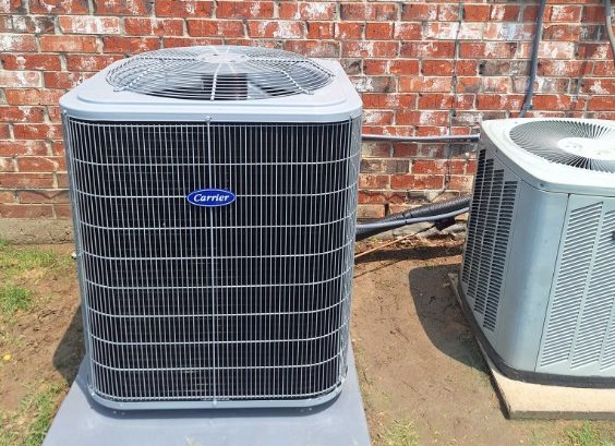 Newly installed Carrier condenser beside an older unit against a brick wall