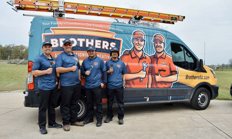 Four Brothers Air Conditioning & Heating technicians in company polo shirts holding wrenches beside a branded service van in Carrollton, Texas