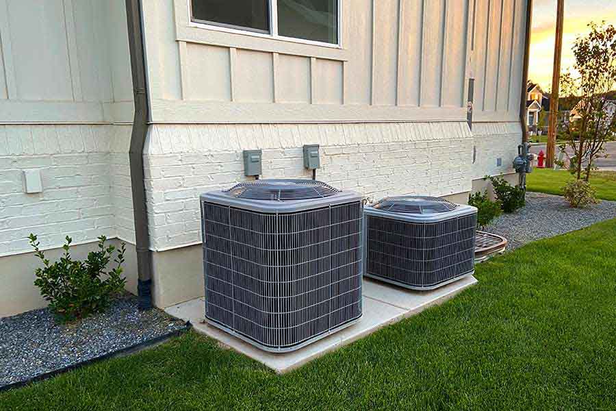 Two air conditioning condensers on a concrete pad beside a newly built home