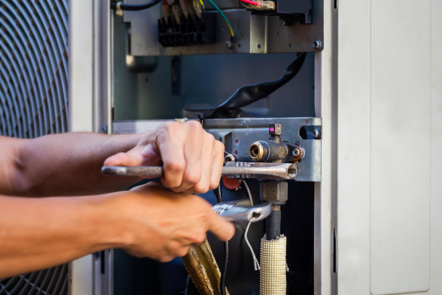 Technician using a wrench inside an open condenser cabinet