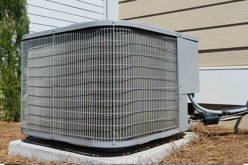 Outdoor condenser with a wire coil guard beside a home