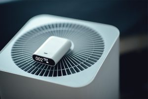 Portable air quality sensor reading PM2.5 resting on top of a home air purifier
