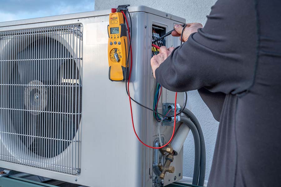 Technician using a multimeter on the electrical panel of an outdoor unit