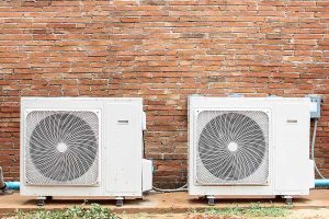 Two mini split outdoor condensers mounted side by side against a brick wall